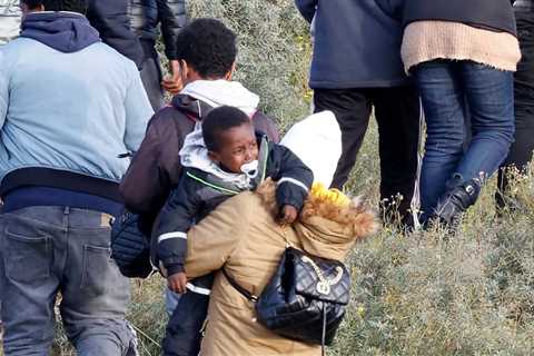 Moment crying tot sucking dummy carried across sand dunes in France as 200 migrants try to cross..