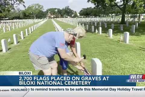 Volunteers place flags on gravesites at Biloxi National Cemetery